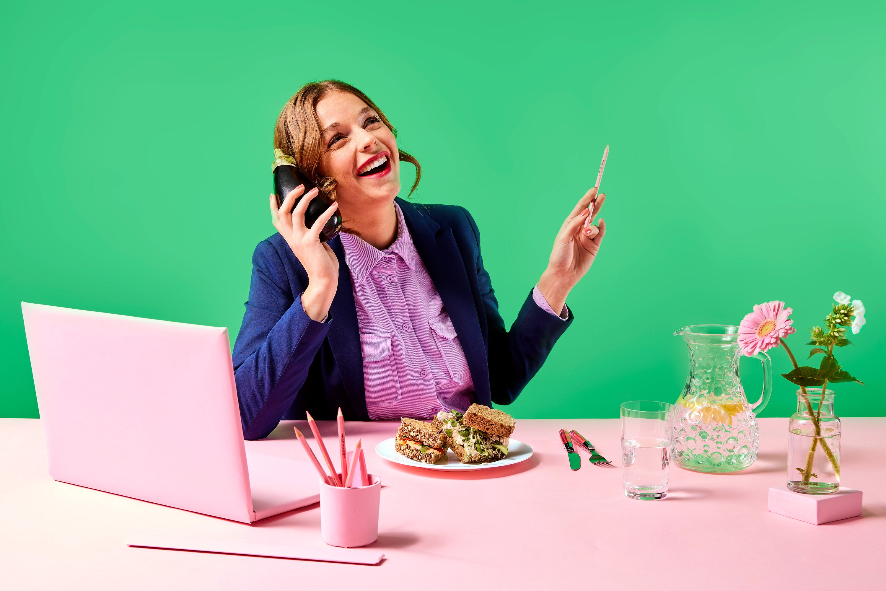 vrouw in kleurrijke kantooromgeving die met aubergine lachend en energiek aan het bellen is, yummiz, vegetarisch